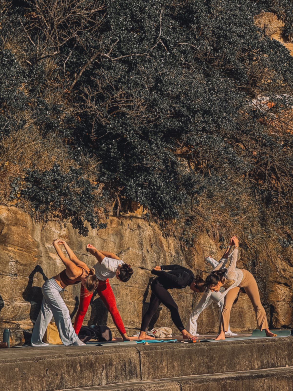 Ella Yoga class stretching against the sandstone cliff at Bondi, Sydney