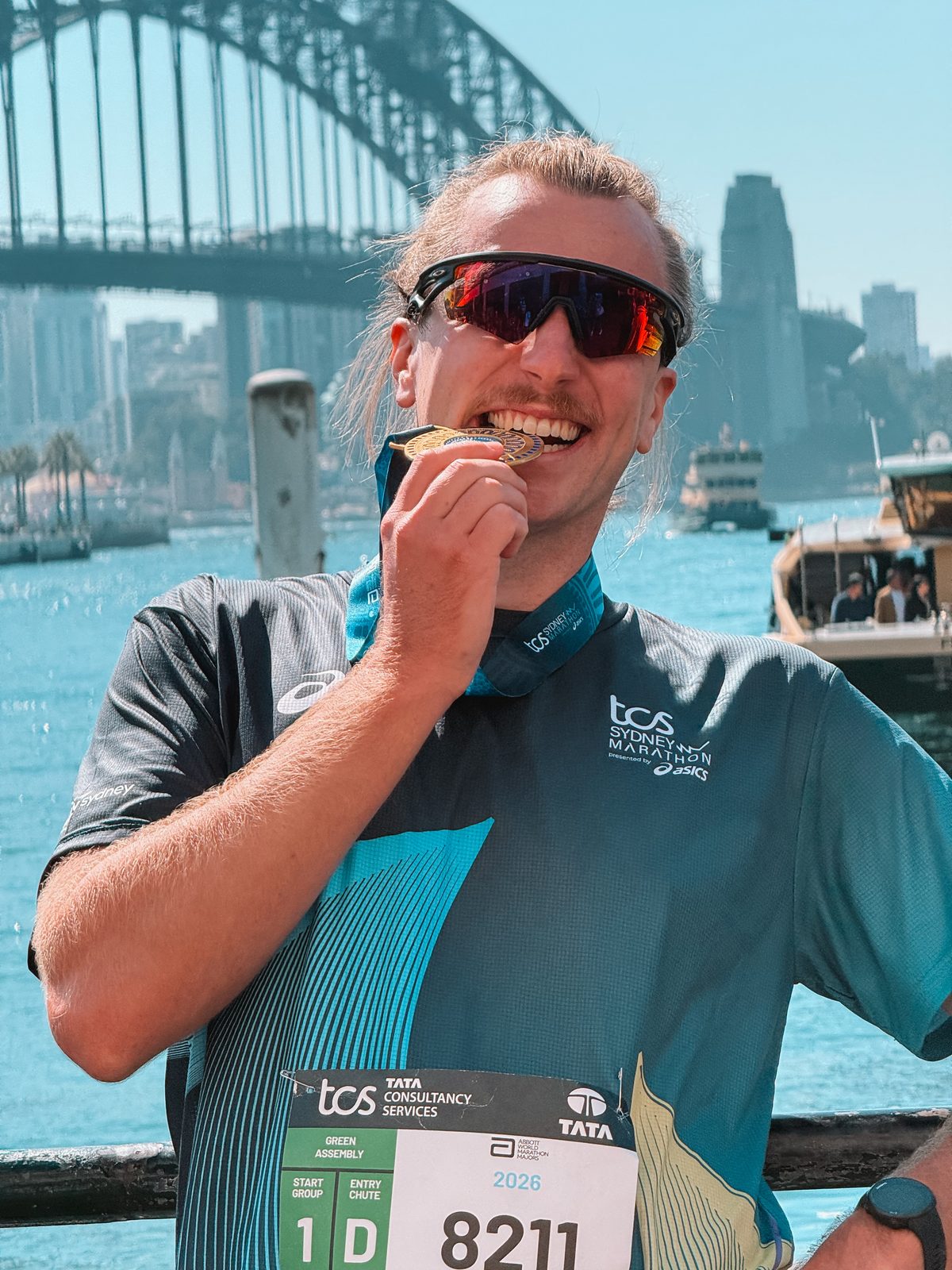 Sydney Marathon finisher biting the medal, Harbour Bridge behind