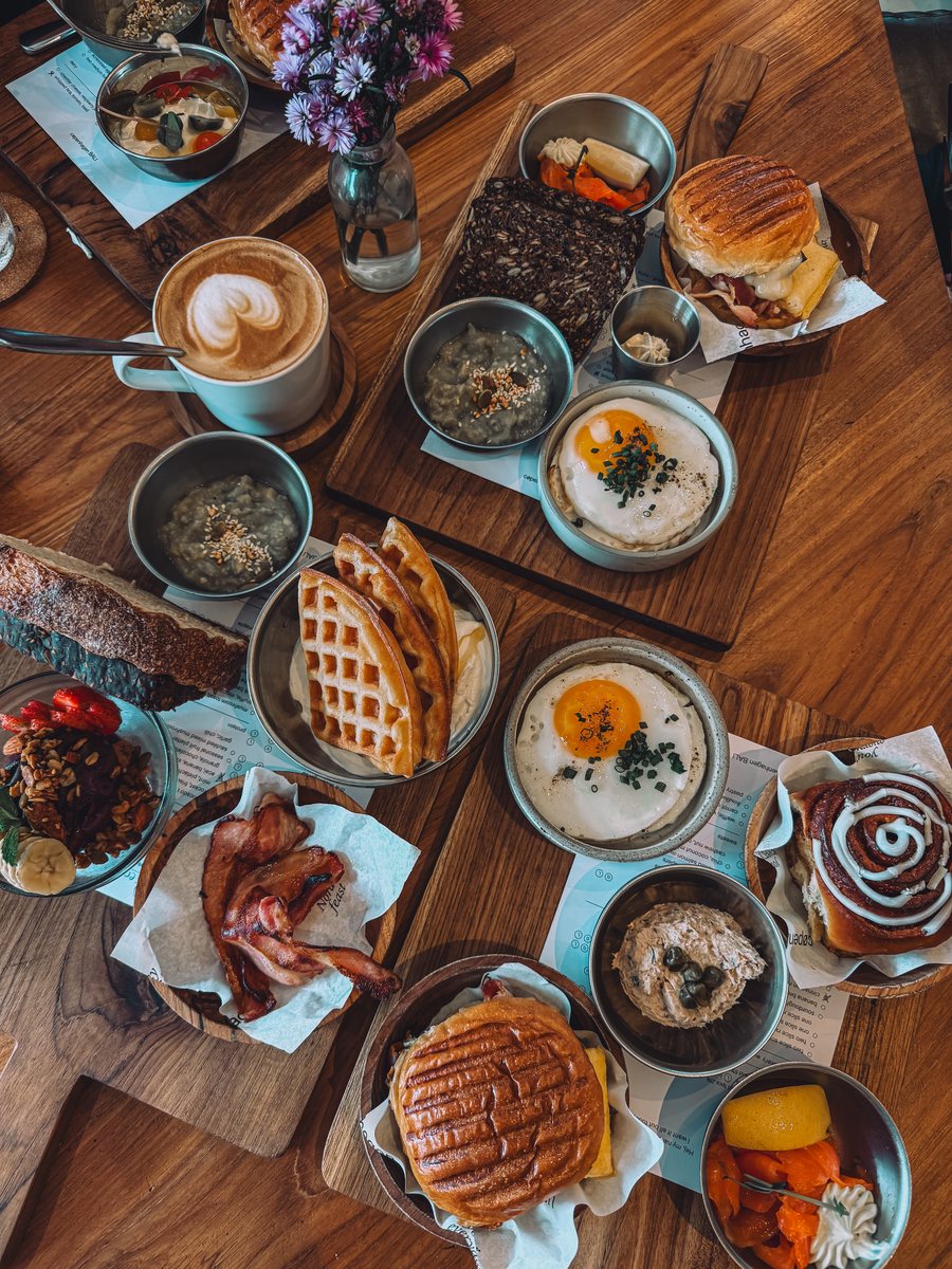 Une table de brunch vue du dessus : gaufres, œufs, bacon, café et brioche à la cannelle