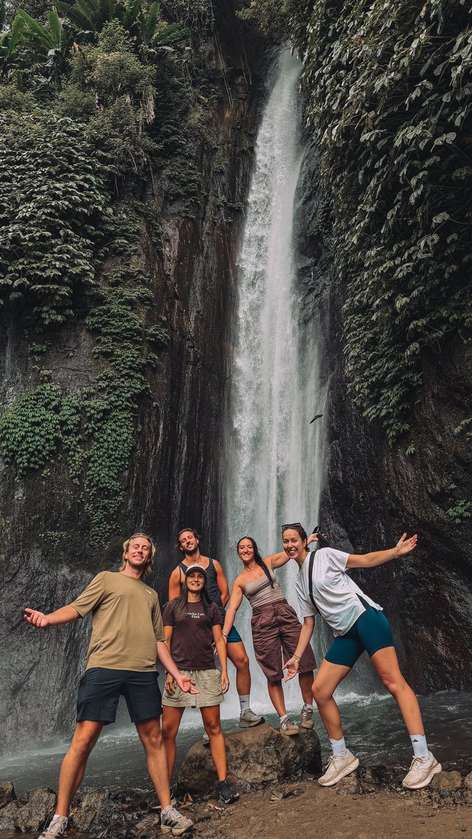 Un groupe de voyageurs au pied d'une haute cascade encaissée dans la végétation