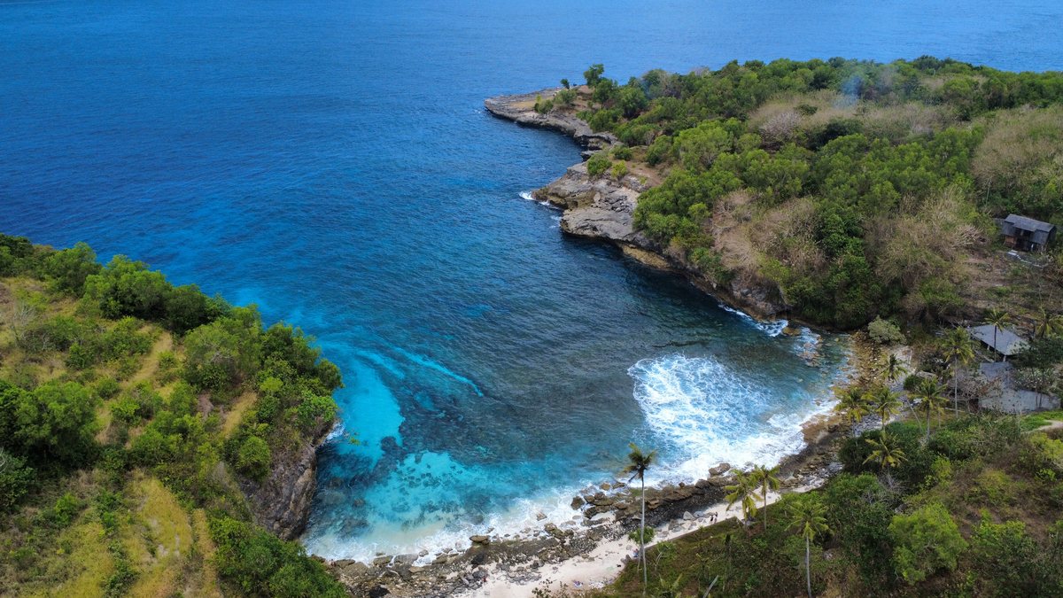 Vue aérienne d'une crique turquoise bordée de falaises et de végétation