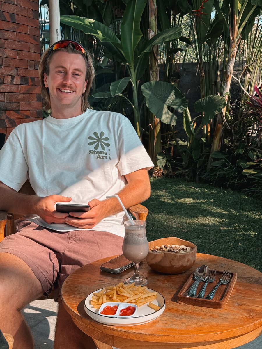 Julien attablé dans un jardin tropical, frites et smoothie devant lui