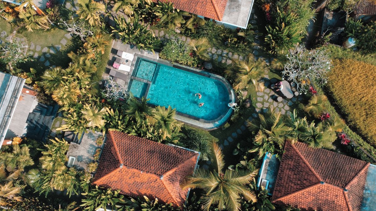 Villa et sa piscine au milieu des toits de tuiles et des palmiers, vue du ciel
