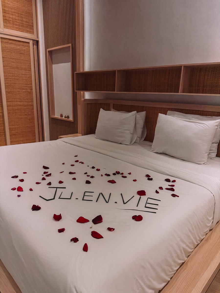 Un lit d'hôtel où des pétales de rose forment le mot Ju.en.vie