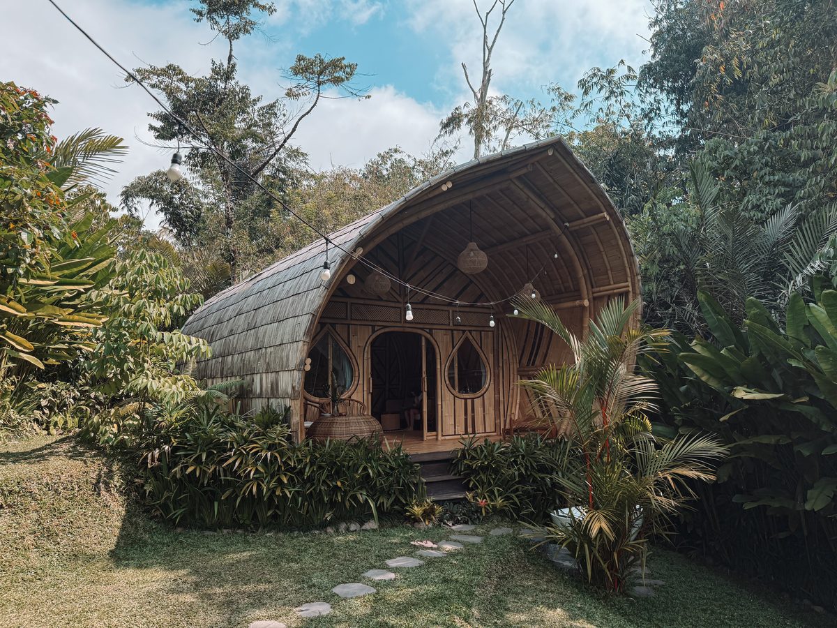 Maison en bambou au toit arrondi, posée dans la jungle et bordée de guirlandes