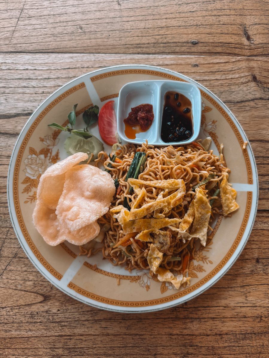 Assiette de mie goreng avec un krupuk et des condiments, sur une table en bois