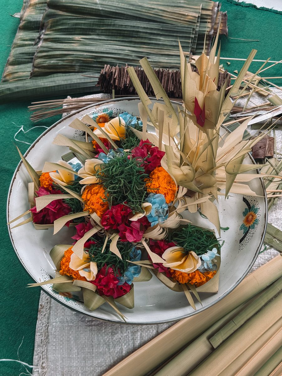 Des offrandes en fleurs et en feuilles de palmier en cours de confection sur un plateau