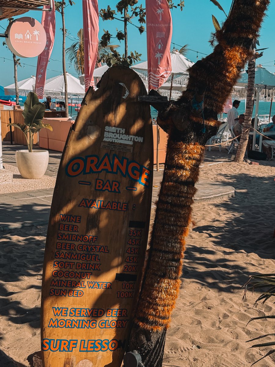 Une planche de surf peinte à la main servant de carte des boissons, plantée dans le sable d'une plage