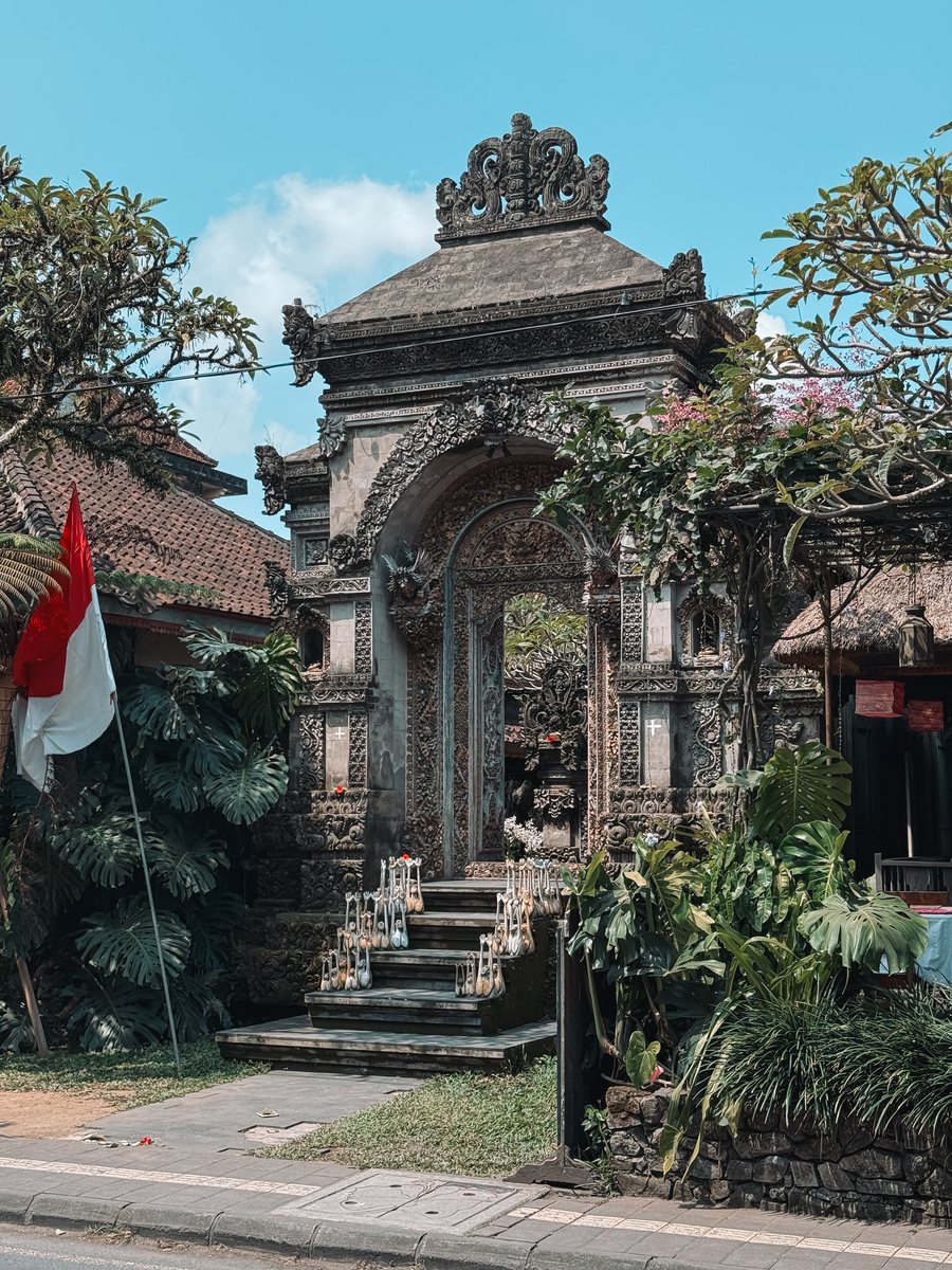 Portail de temple balinais en bord de route, drapeau indonésien planté devant