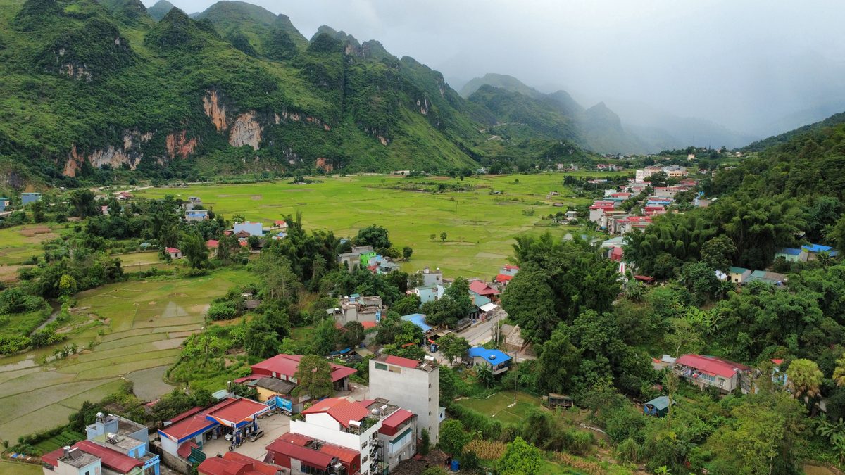 Un village aux toits rouges au milieu des rizières, cerné par les montagnes, vu du ciel