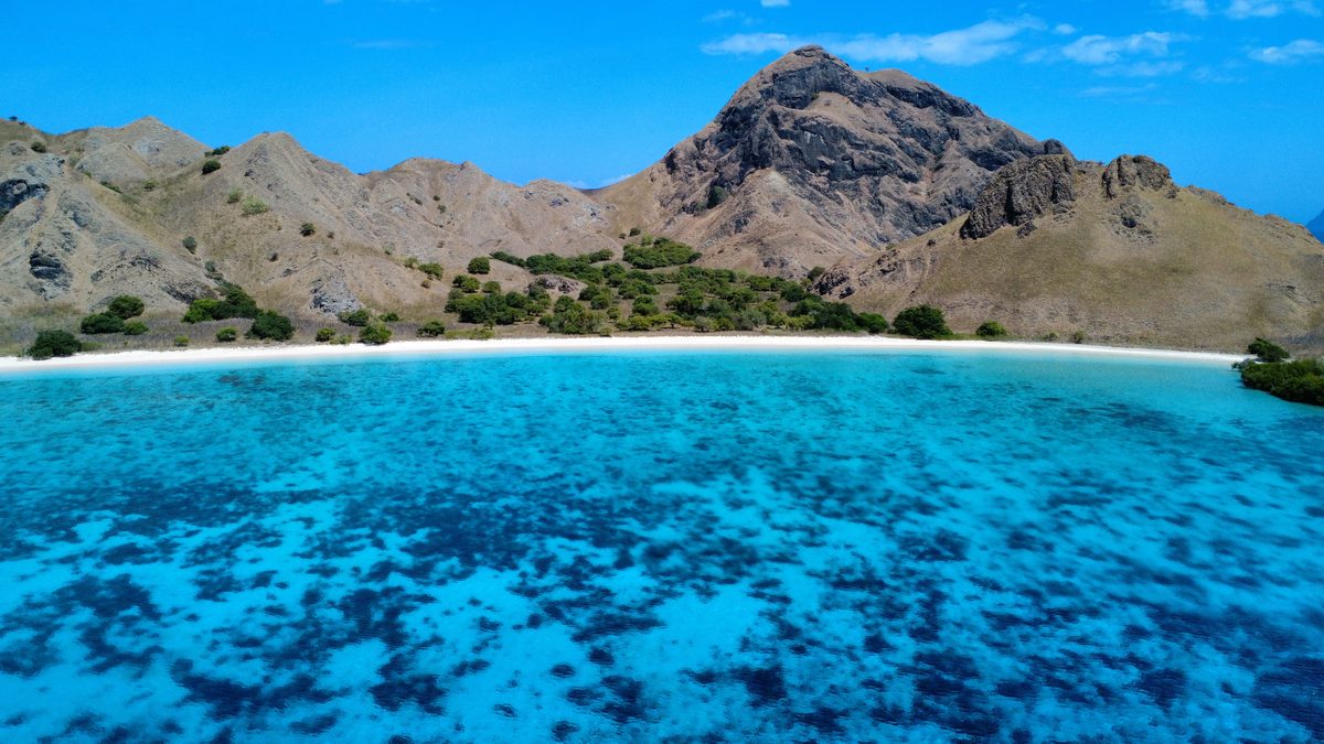 Une crique aux eaux turquoise bordée de collines sèches, vue du ciel