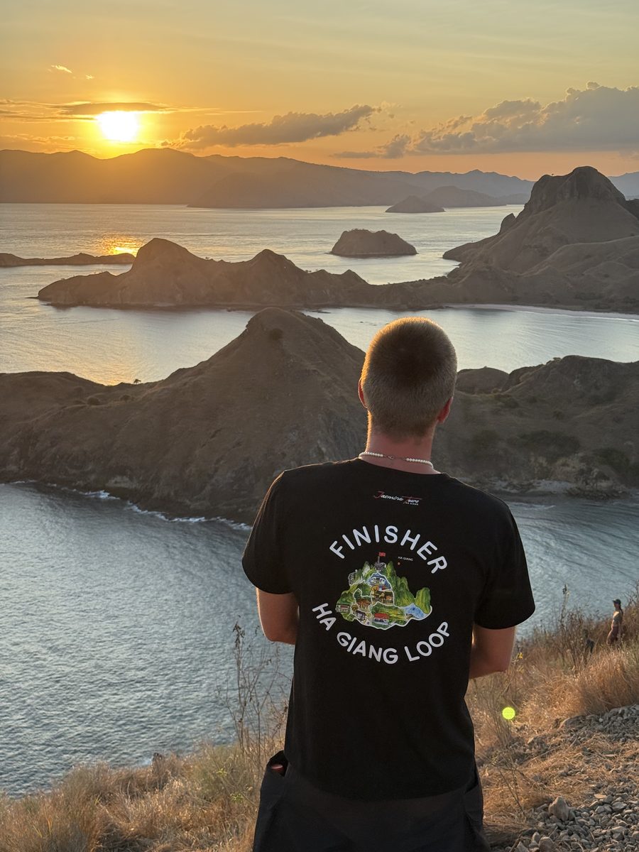 Julien de dos au sommet de Padar, en t shirt Finisher de la boucle de Ha Giang, face aux baies au soleil bas