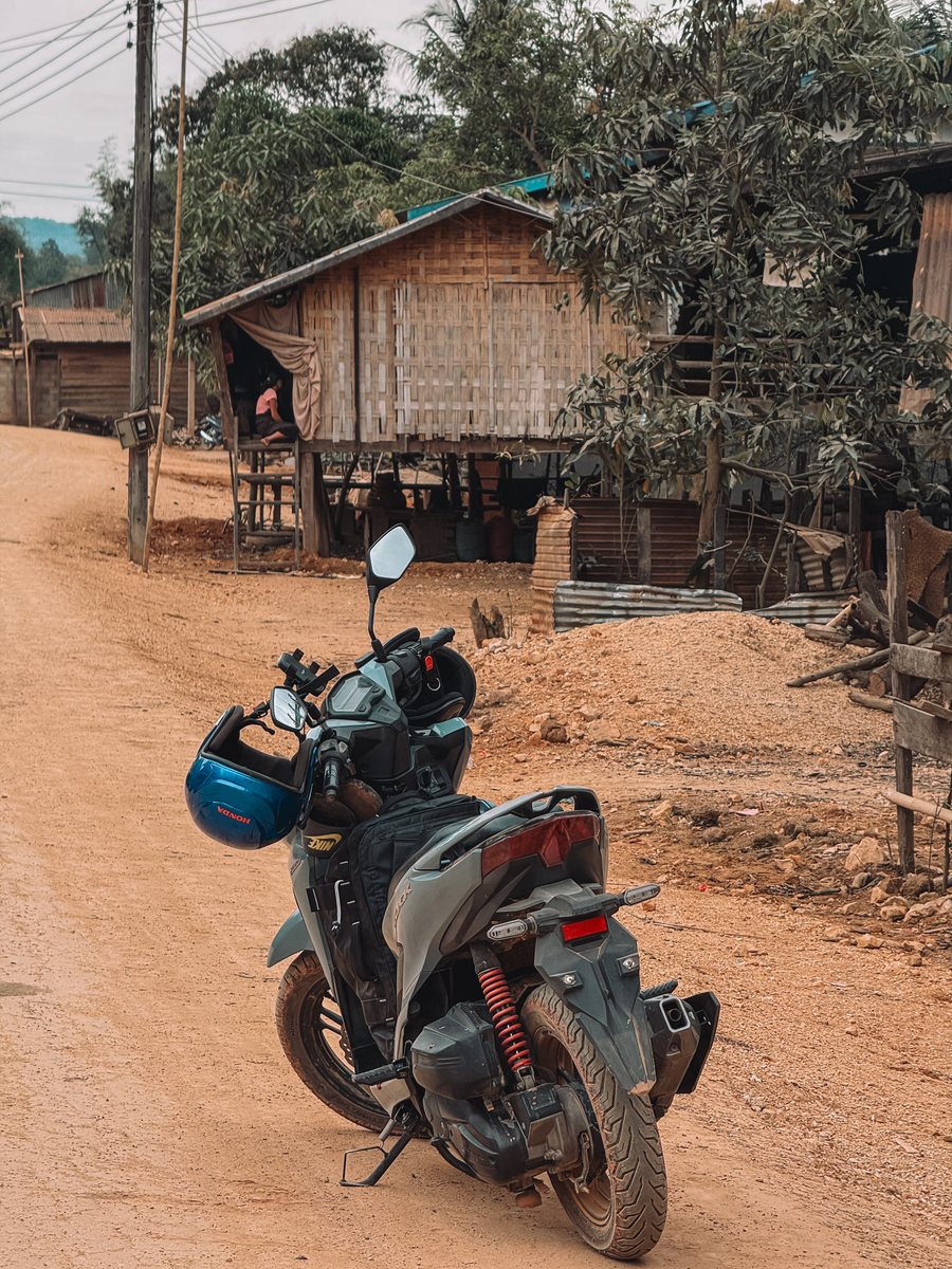 Scooter chargé garé sur une piste de terre, devant des maisons sur pilotis