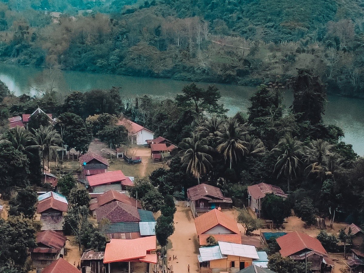 Village laotien aux toits de tôle rouge, au bord d'une rivière, vu du ciel