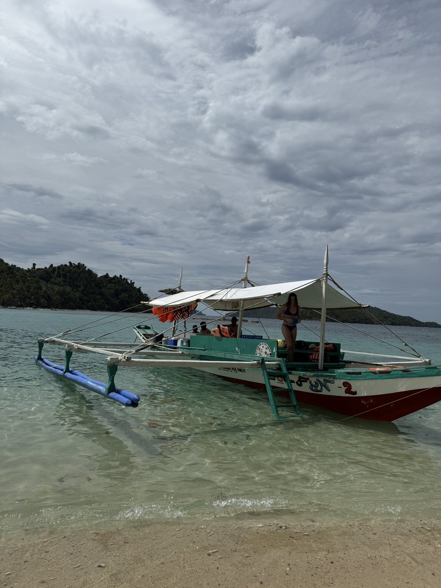 Bangka vert et blanc échoué sur une plage, sous un ciel couvert