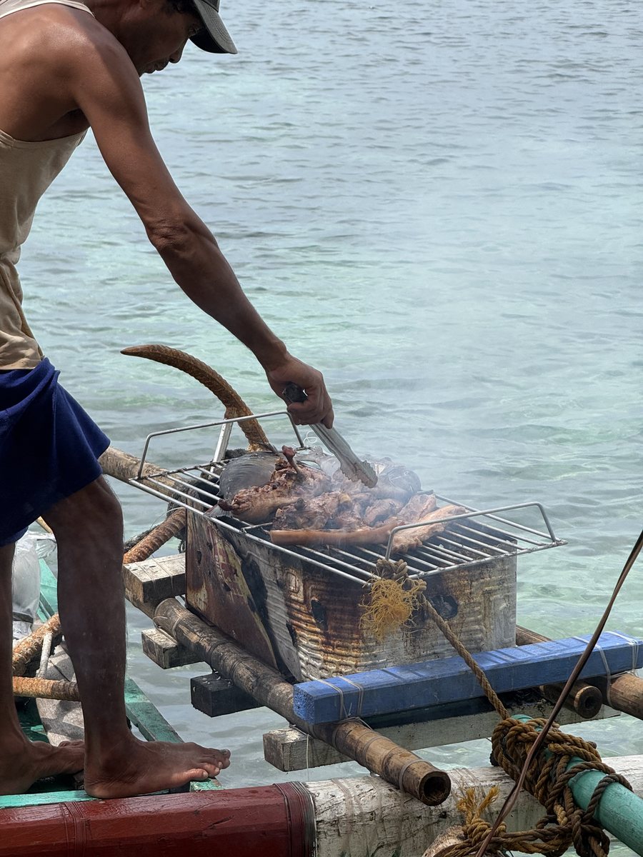 Homme qui retourne des brochettes sur un barbecue posé à l'arrière d'un bateau