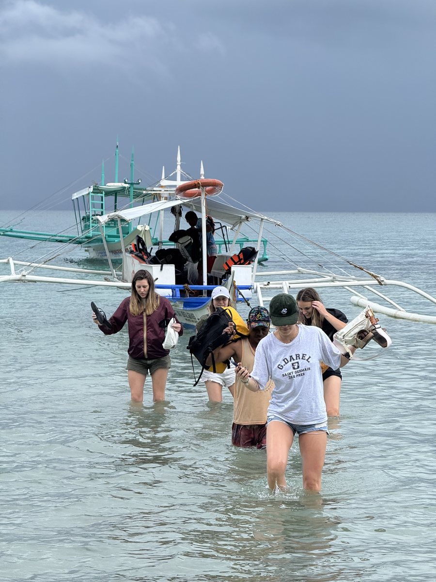 Groupe de voyageurs qui débarque d'un bangka, les jambes dans l'eau, sous un ciel d'orage