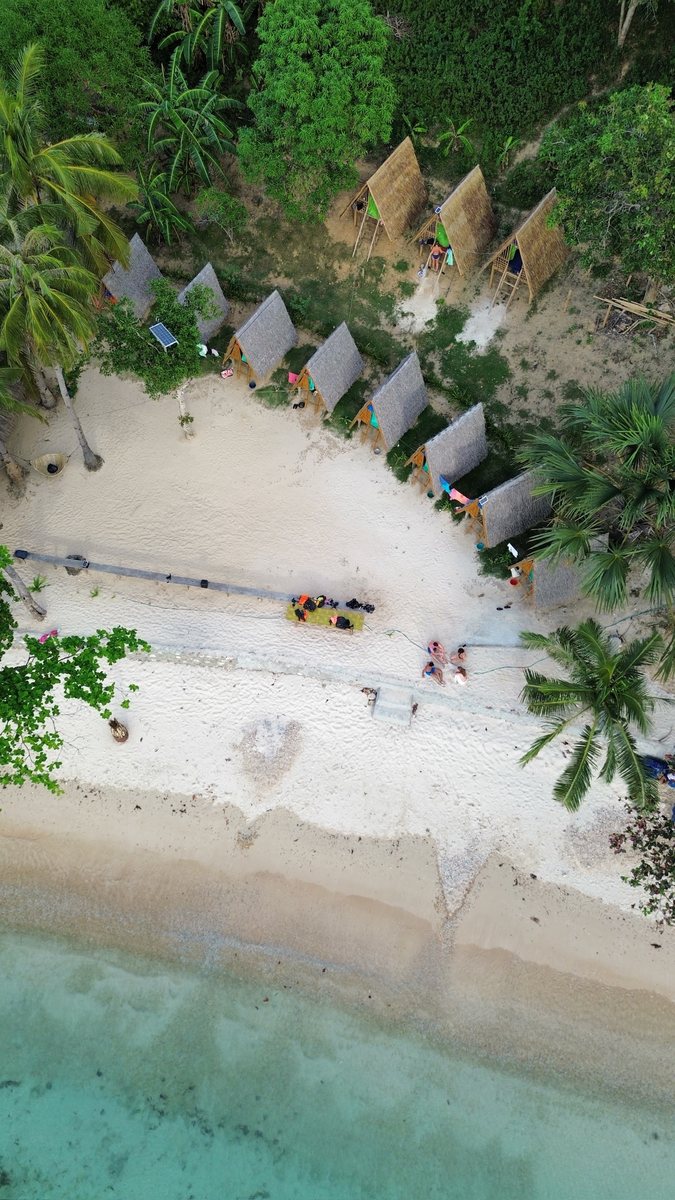 Rangée de huttes de bivouac alignées en haut d'une plage, vue du ciel