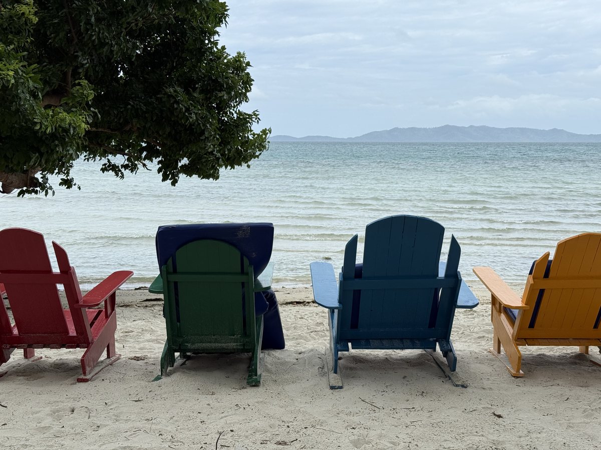 Quatre fauteuils de plage colorés tournés vers la mer et les îles au loin