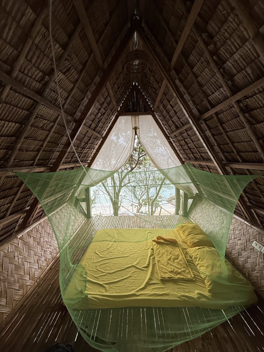 Intérieur d'une hutte en bambou : un matelas sous une moustiquaire, ouvert sur la mer