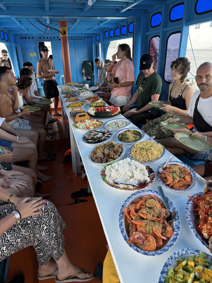 Longue tablée de voyageurs autour d'un buffet de crevettes et de plats servis à bord