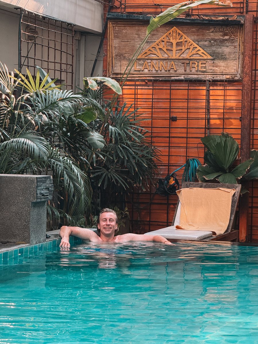 Julien dans la piscine d'un hôtel de Chiang Mai, façade en bois derrière