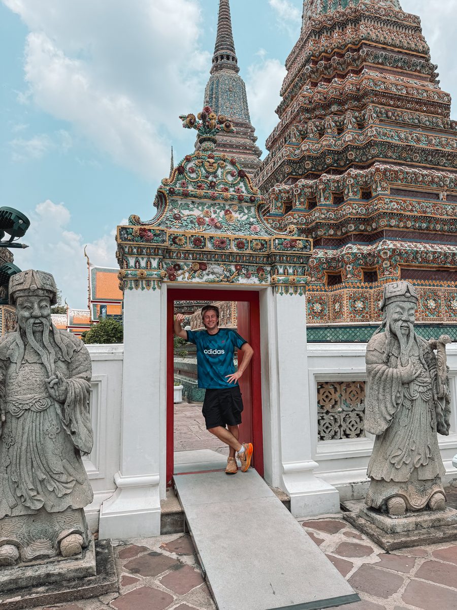 Julien dans une porte rouge du Wat Pho, entre deux gardiens de pierre