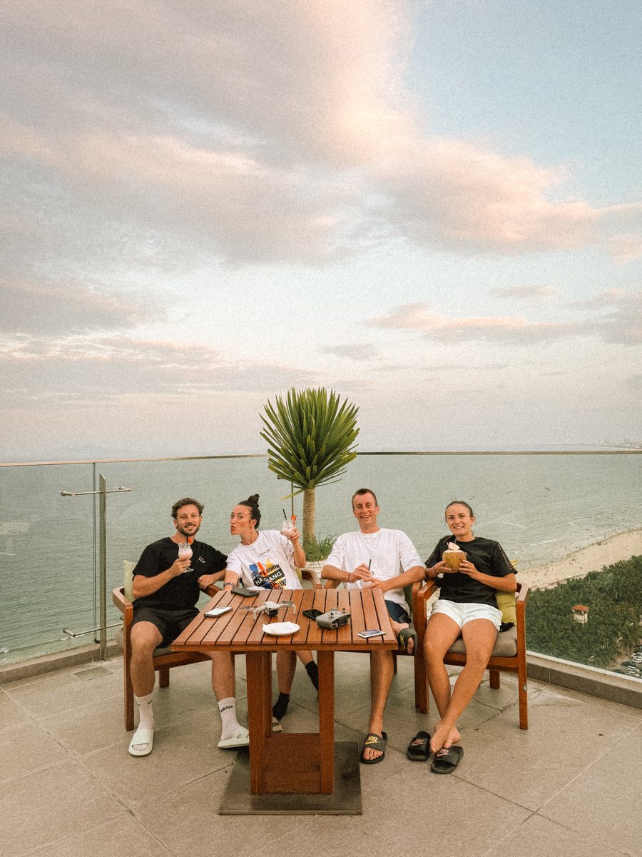 Quatre voyageurs attablés sur une terrasse face à la mer, au coucher du soleil