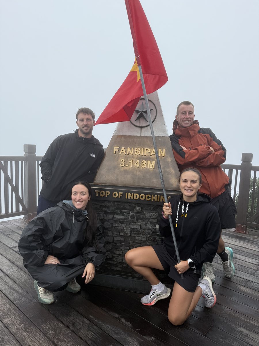 Groupe de quatre voyageurs devant la borne du sommet du Fansipan, à trois mille cent quarante trois mètres