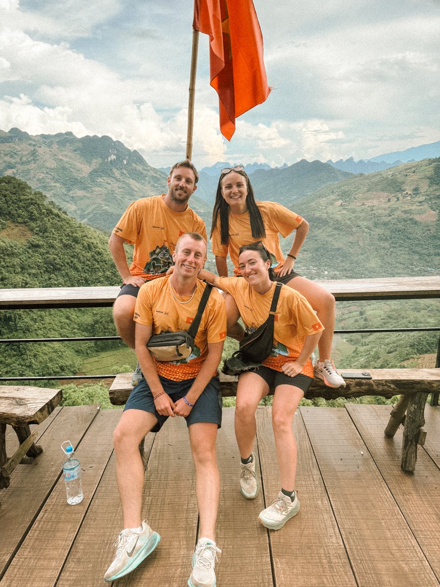 Groupe de voyageurs en t shirts orange devant un drapeau vietnamien, les montagnes de Ha Giang derrière