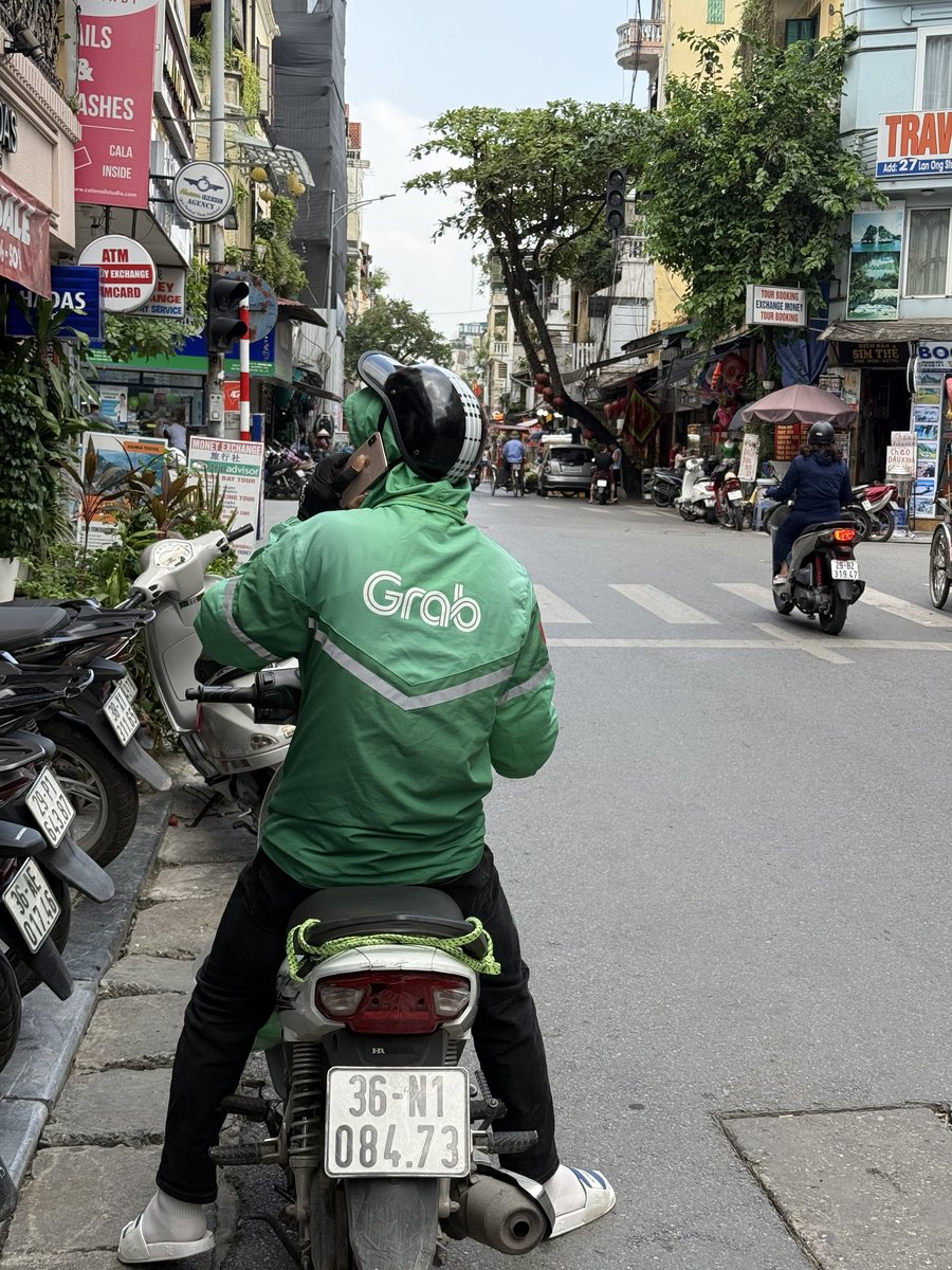Chauffeur en veste verte Grab arrêté dans une rue étroite de Hanoi