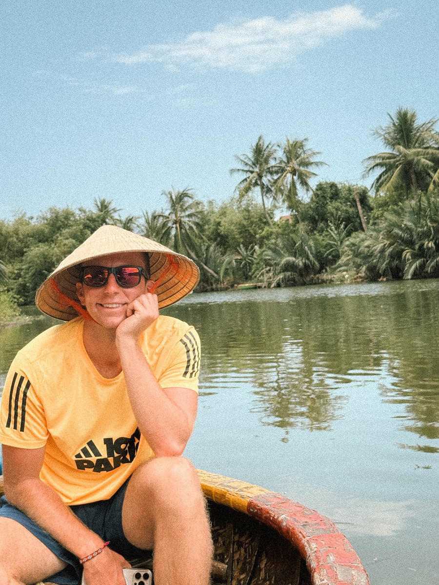 Julien coiffé d'un chapeau conique dans une barque, sur une rivière bordée de cocotiers