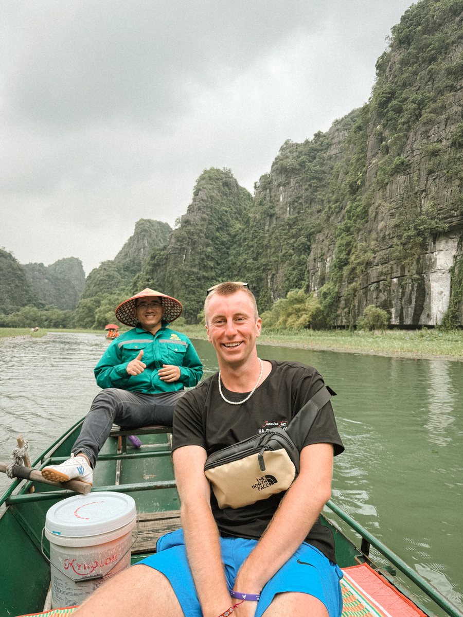 Julien en barque sur une rivière bordée de pitons calcaires, avec une batelière au chapeau conique