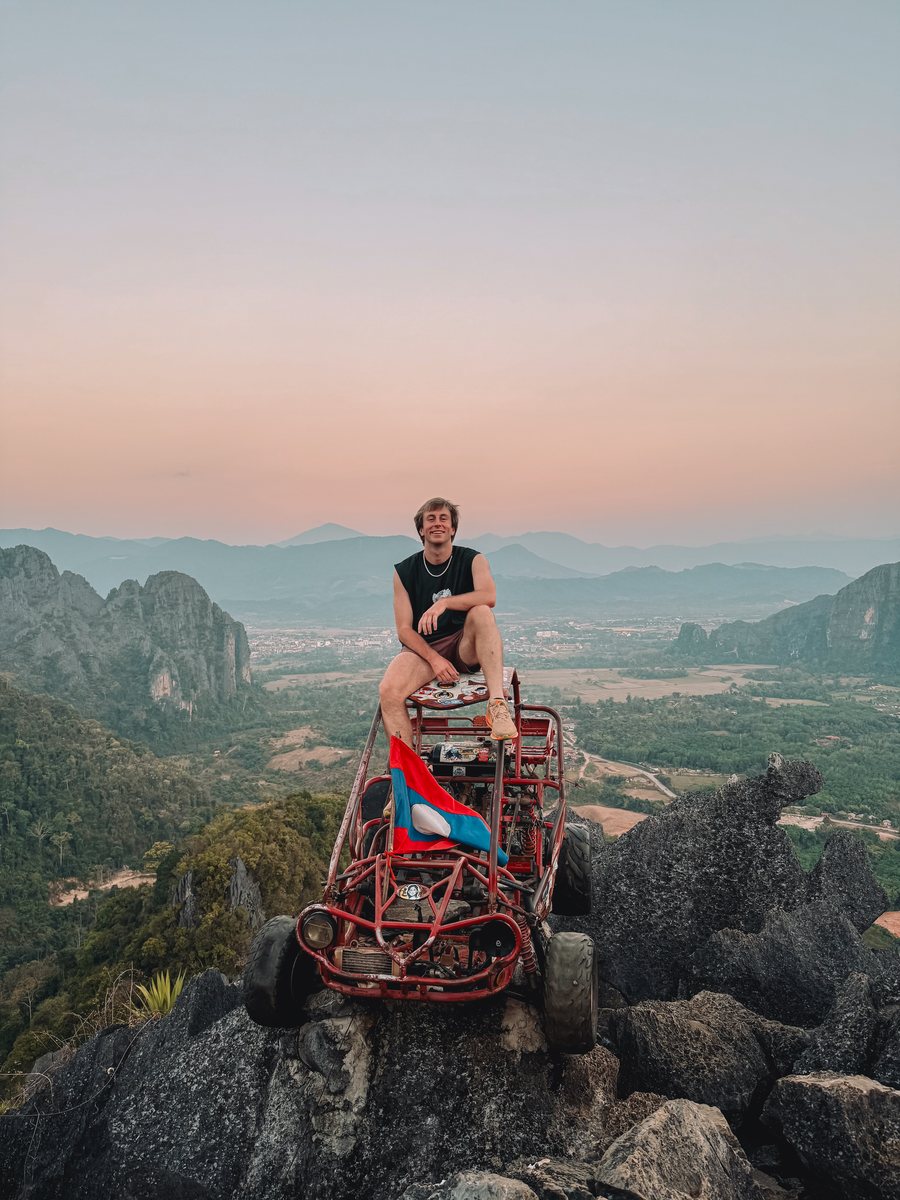 Julien assis sur un buggy au sommet d'un piton rocheux, au coucher du soleil à Vang Vieng